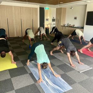 A group of office employees participating in a corporate yoga session doing downward facing dog